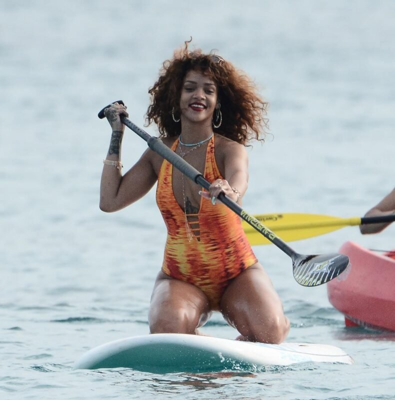 Rihanna paddleboarding in an orange swimsuit